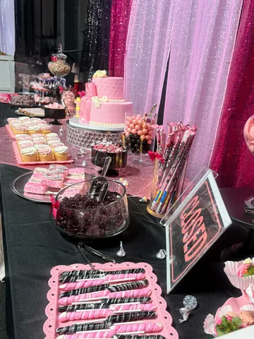 Pink themed candy and dessert table with tiered cake, chocolate-dipped pretzels, candy jars and custom signage